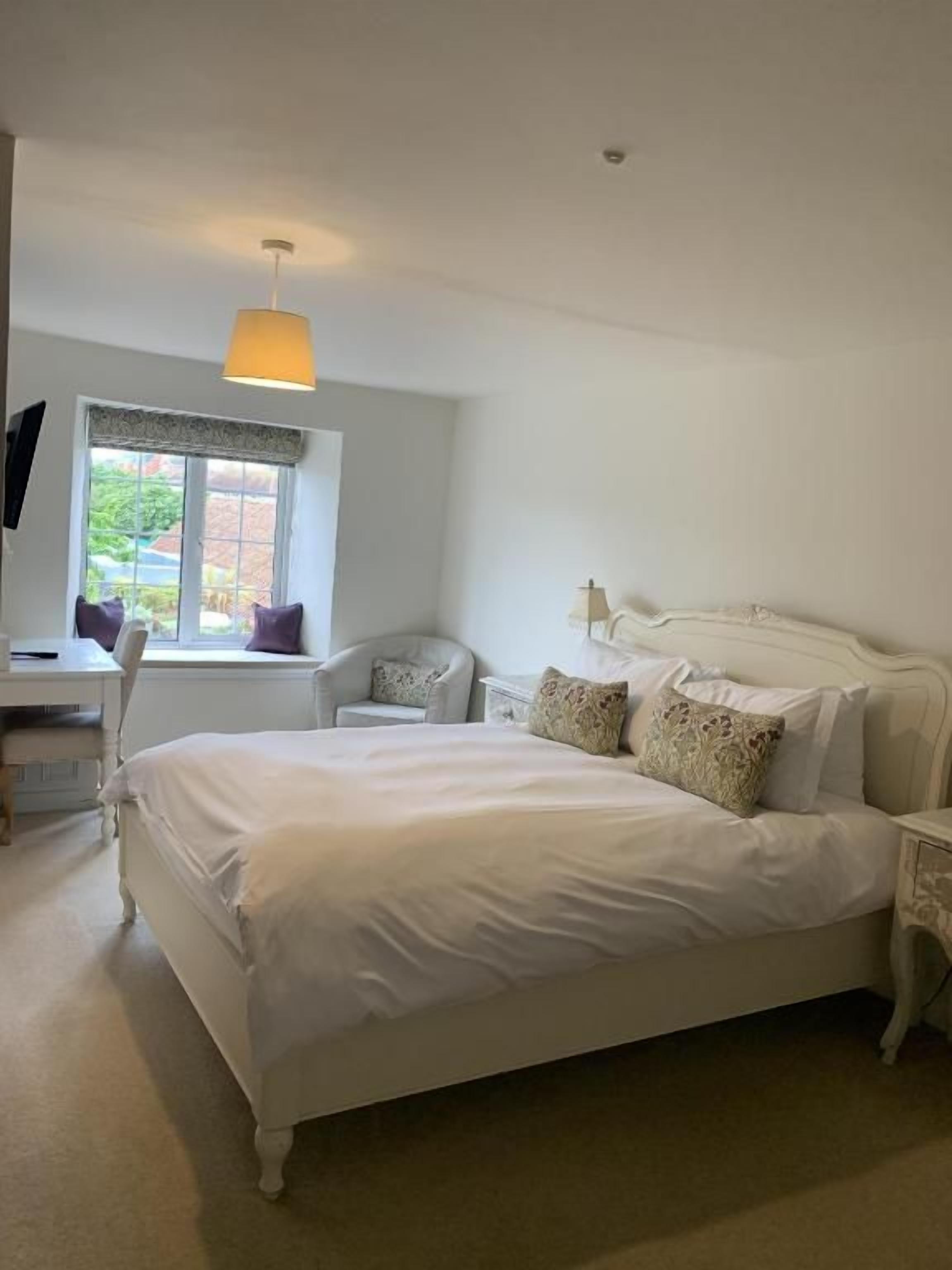 A bedroom with a large bed, a desk, a chair, and a window with a view.