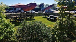 A picnic area with tables and umbrellas, surrounded by greenery and a parking lot in the background. - The White Horse Inn (Cambridge)