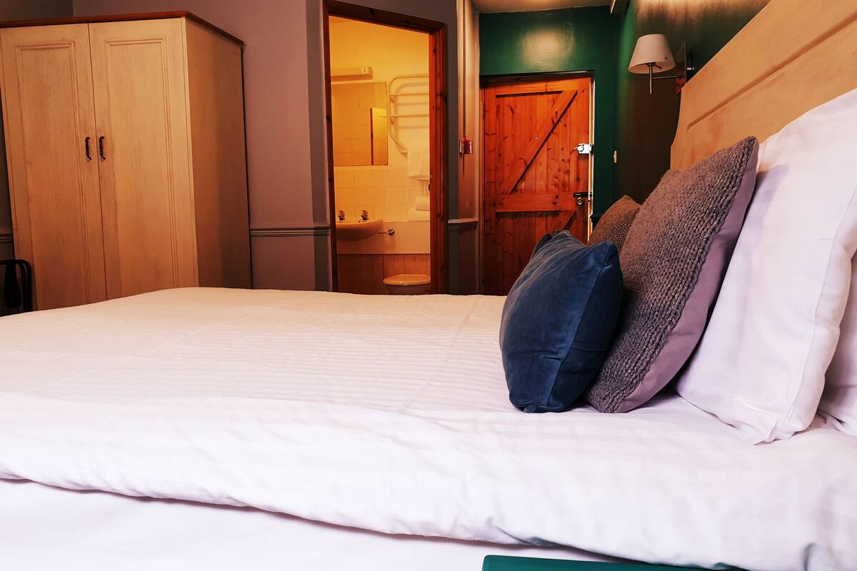 A neatly made bed with white linens and a green headboard.