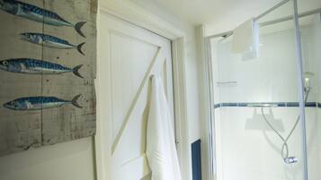A bathroom with a glass shower enclosure, a wooden door with a towel hanging, and a wall with fish paintings.