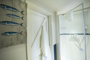 A bathroom with a glass shower enclosure, a wooden door with a towel hanging, and a wall with fish paintings.