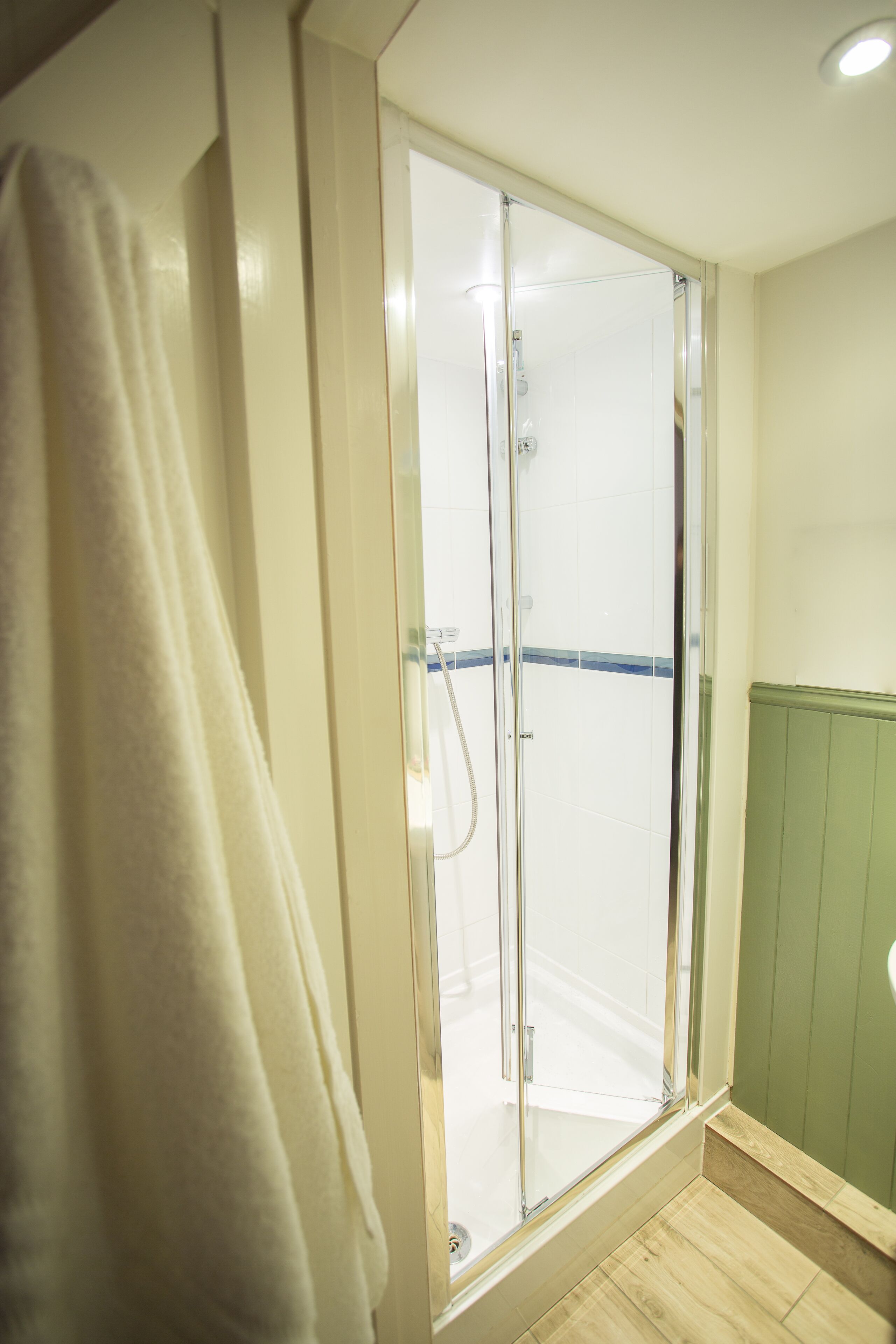 A bathroom with a glass shower enclosure, a white towel hanging on the wall, and a green wall panel.