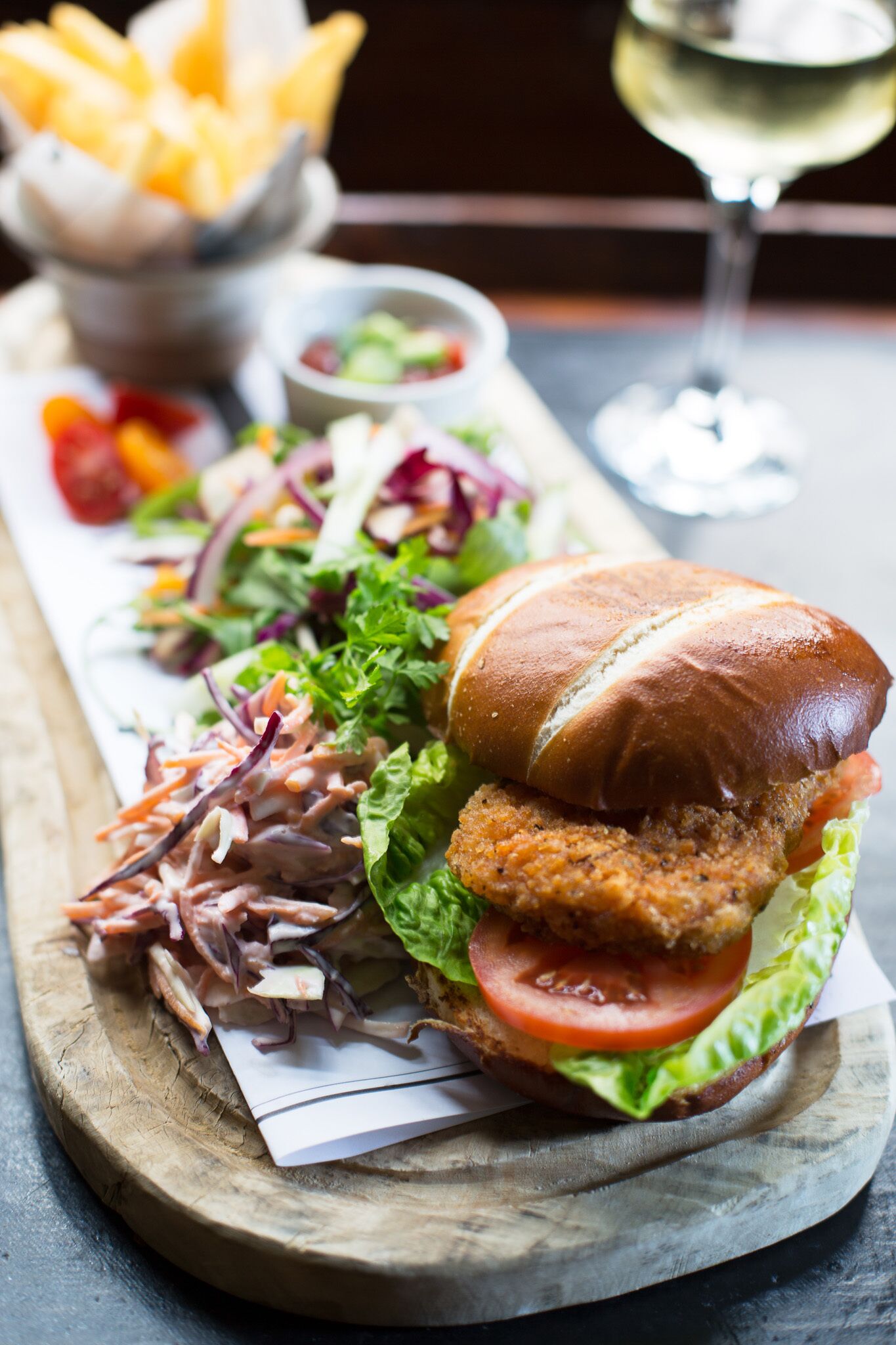 A sandwich with lettuce, tomato, and a side of coleslaw on a wooden board.