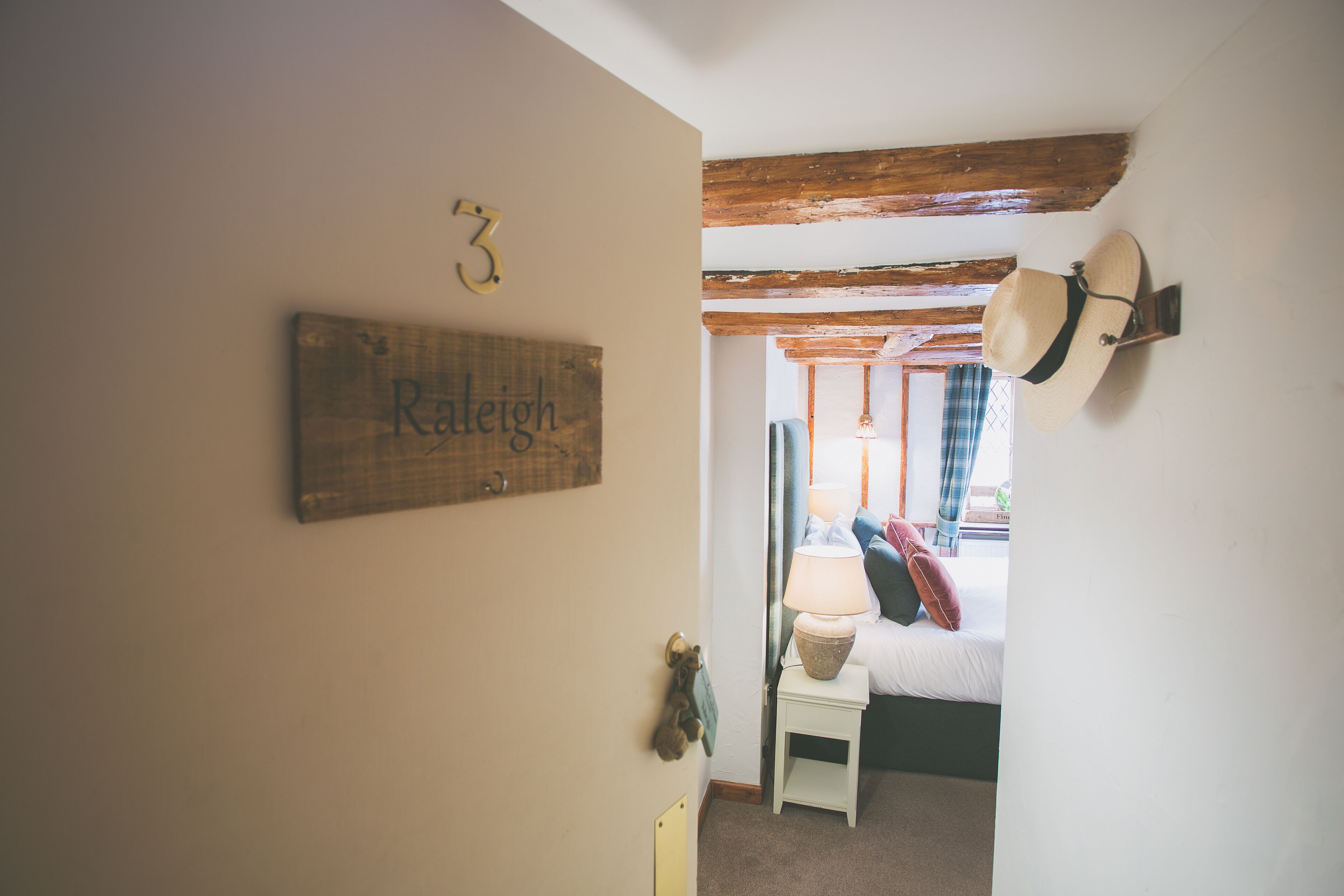 A room with a bed, a small bedside table, a lamp, a hat on the wall, and a sign on the wall.