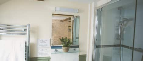 Un baño con cabina de ducha de vidrio, un lavamanos con espejo y un perchero para toallas.