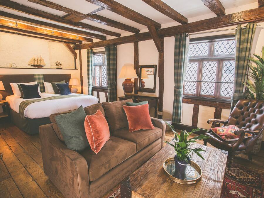 A cozy room with a bed, a brown sofa, a leather armchair, and a wooden coffee table.