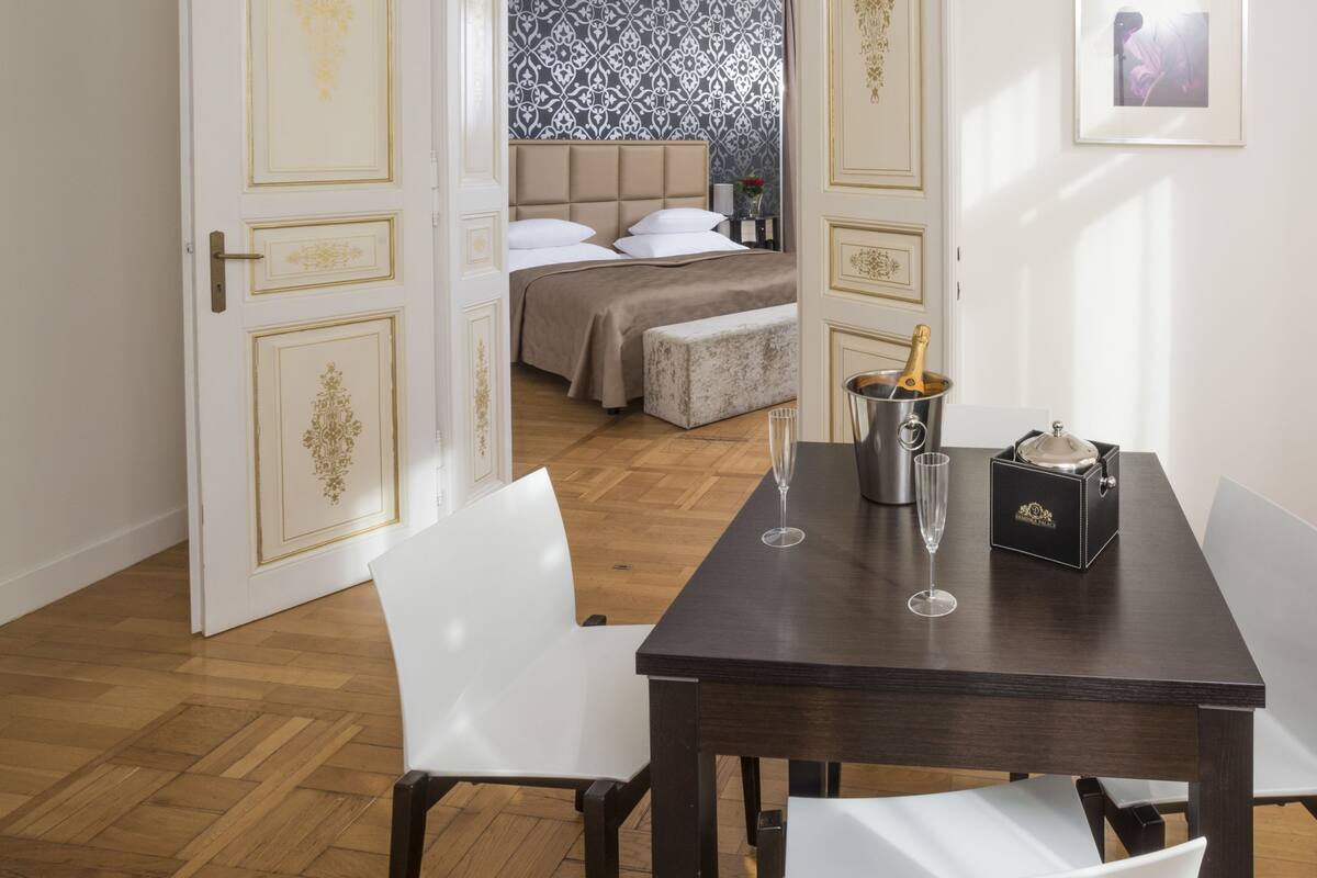 Habitación de hotel con piso de madera, una mesa de comedor con sillas, cama con cabecera estampada y un cuadro en la pared.
