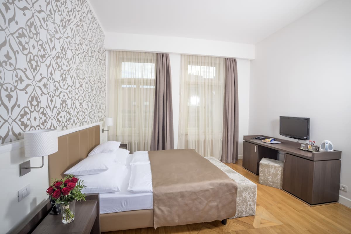 Una habitación de hotel con cama, escritorio, televisor y ventana con cortinas.
