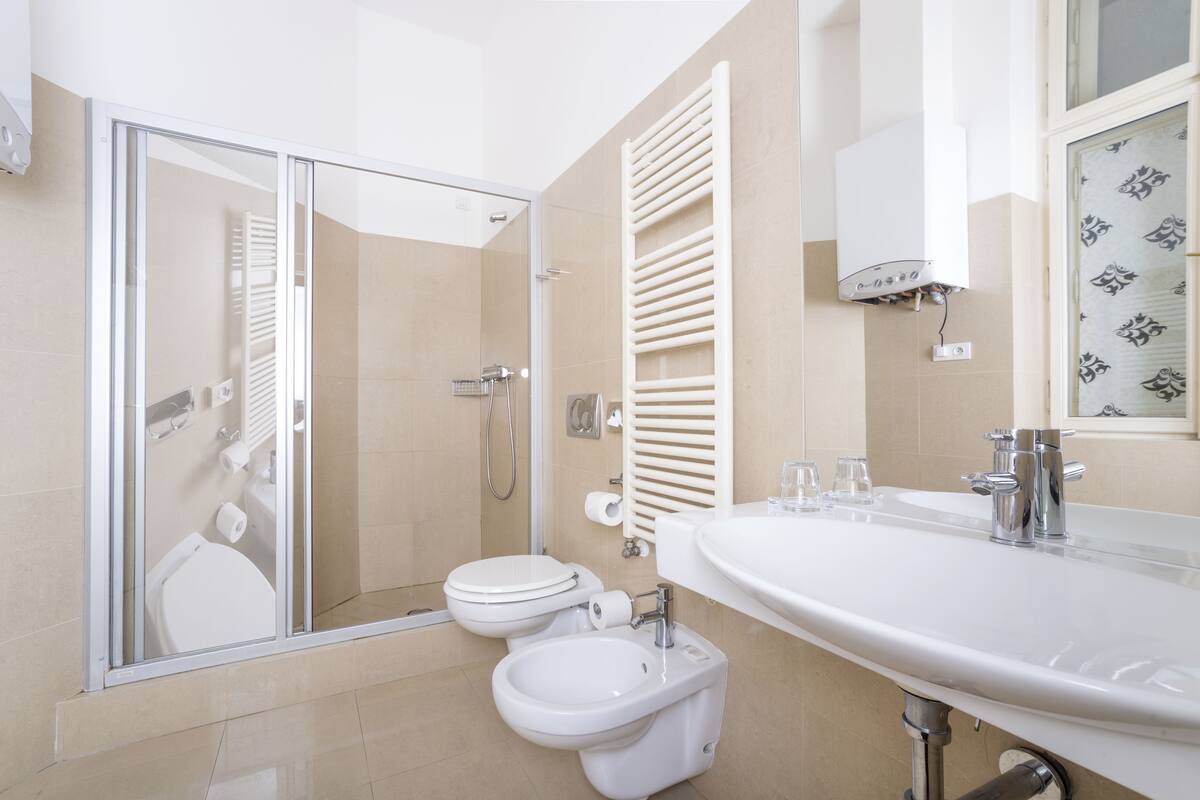 Un baño moderno con mampara de vidrio, inodoro, bidé y lavamanos con espejo.
