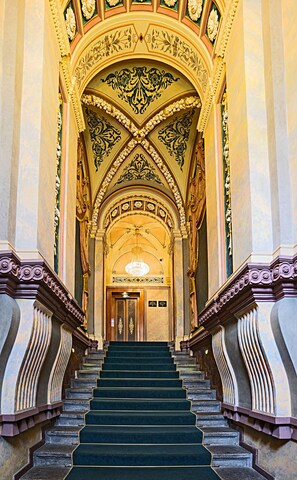 Un magnifique escalier, agrémenté de détails architecturaux raffinés, mène à une entrée somptueuse surmontée d’un lustre.