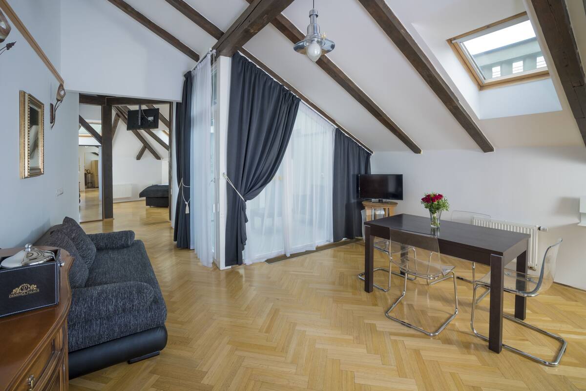 Un loft espacioso con vigas de madera, un comedor con mesa y sillas, un sofá y un televisor.