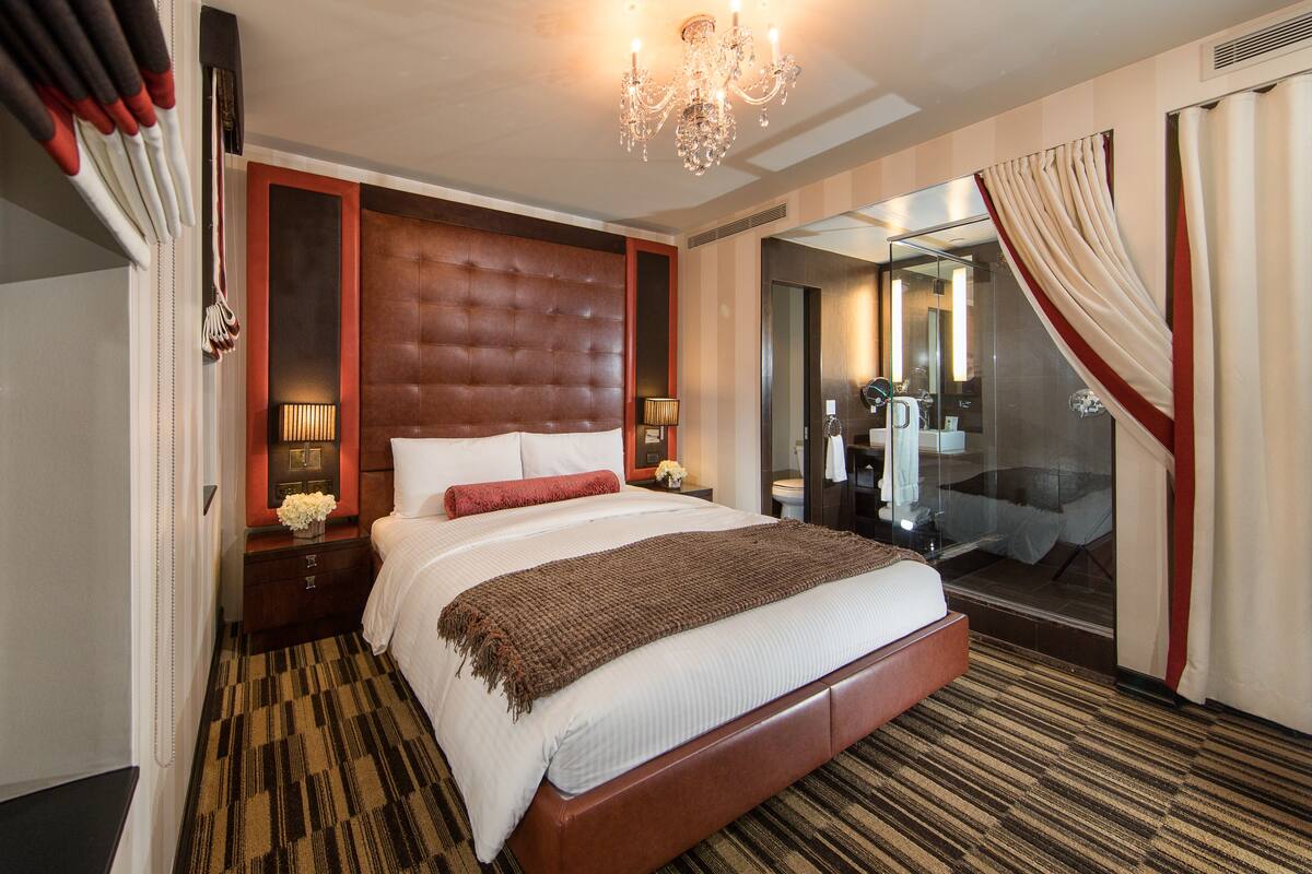 A large bed with a tufted headboard, a chandelier, and a mirror above the bed.