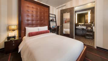 A hotel room with a large bed, a bedside table with a lamp, a wardrobe, and a bathroom visible through an open door.
