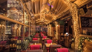 An indoor dining area with tables and chairs, a chandelier, and a view of the cityscape through large windows.