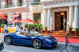 Un coche deportivo descapotable azul estacionado frente a un edificio con toldo rojo y puerta dorada.
