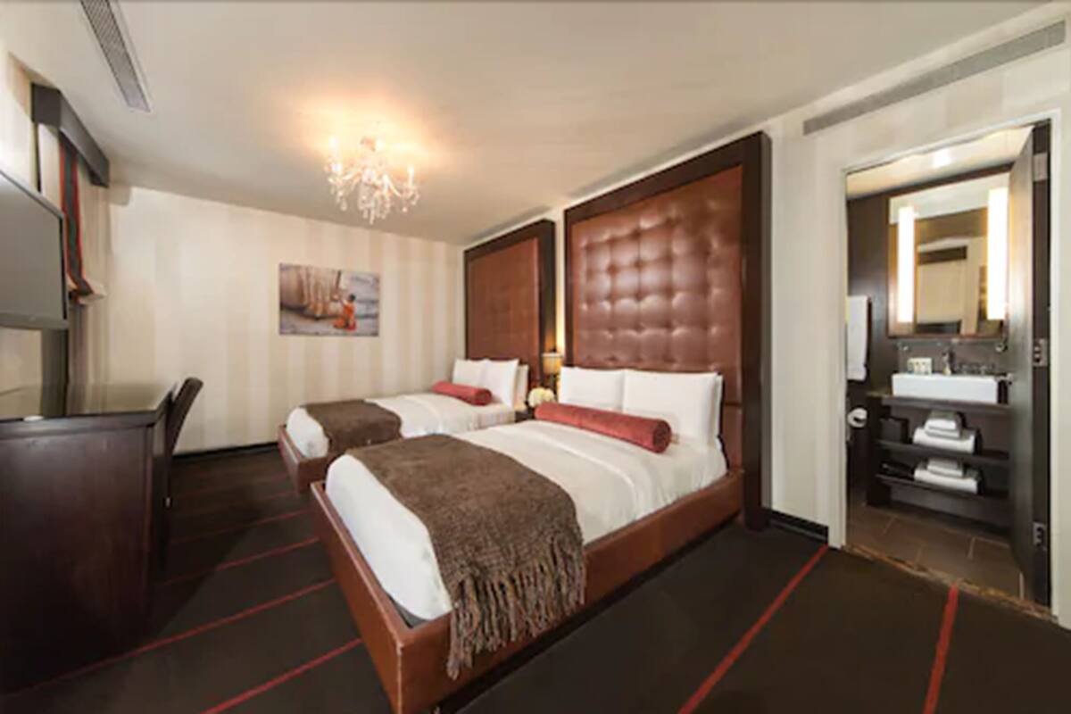 A hotel room with two beds, a desk, a mirror, and a bathroom.