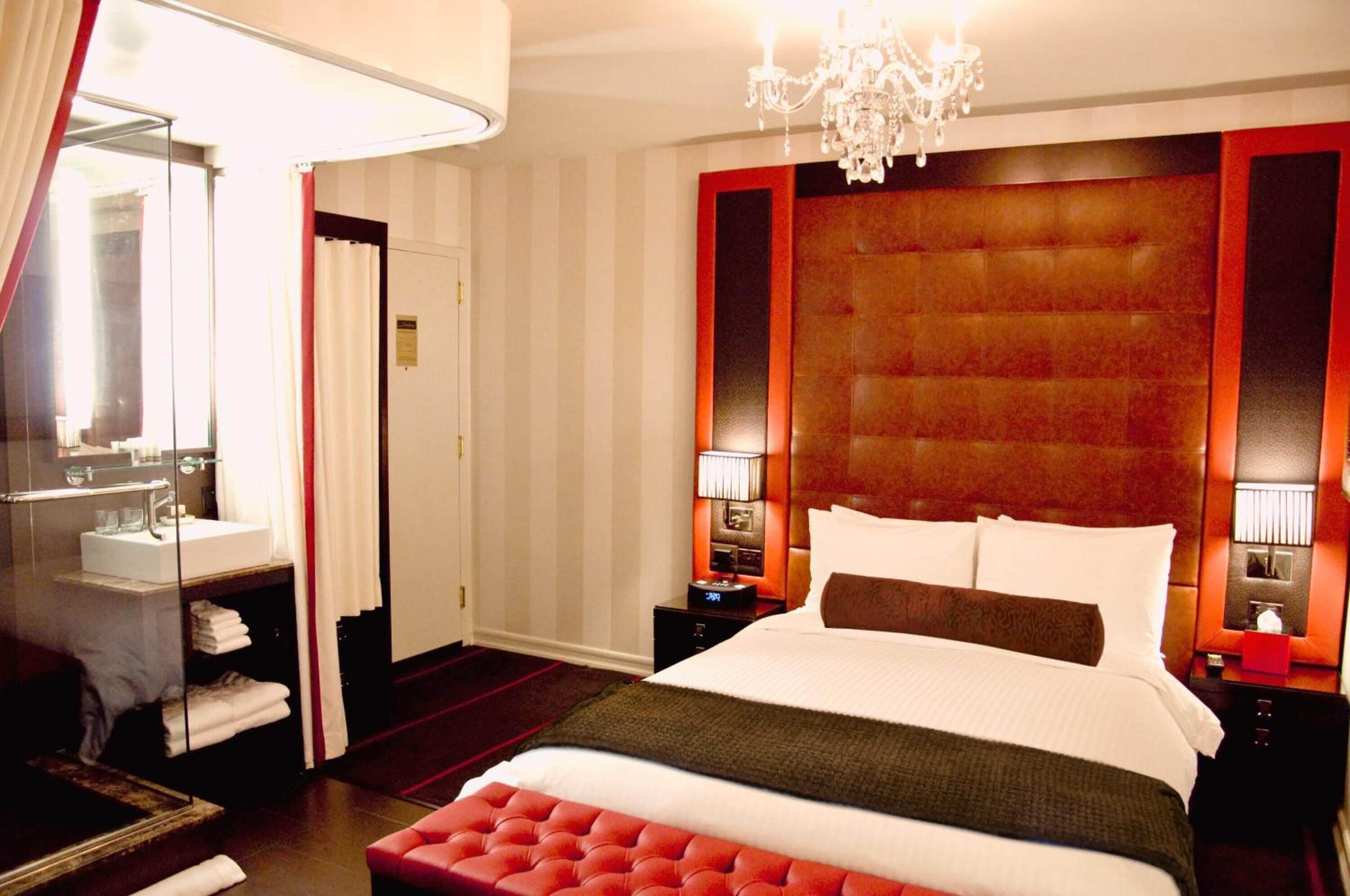 A hotel room with a large bed, a bedside table with a lamp, a mirror, and a red upholstered headboard.
