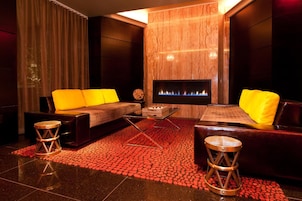 A modern lounge area with a fireplace, leather sofas with yellow cushions, and a patterned red carpet.