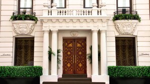 A building with a grand entrance featuring a double door with intricate designs, flanked by columns and topped with a balcony.