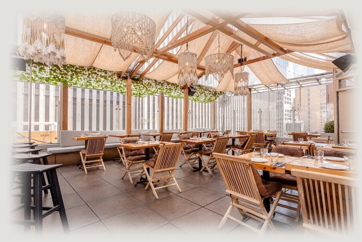 A restaurant with wooden tables and chairs, hanging chandeliers, and a view of buildings through large windows.