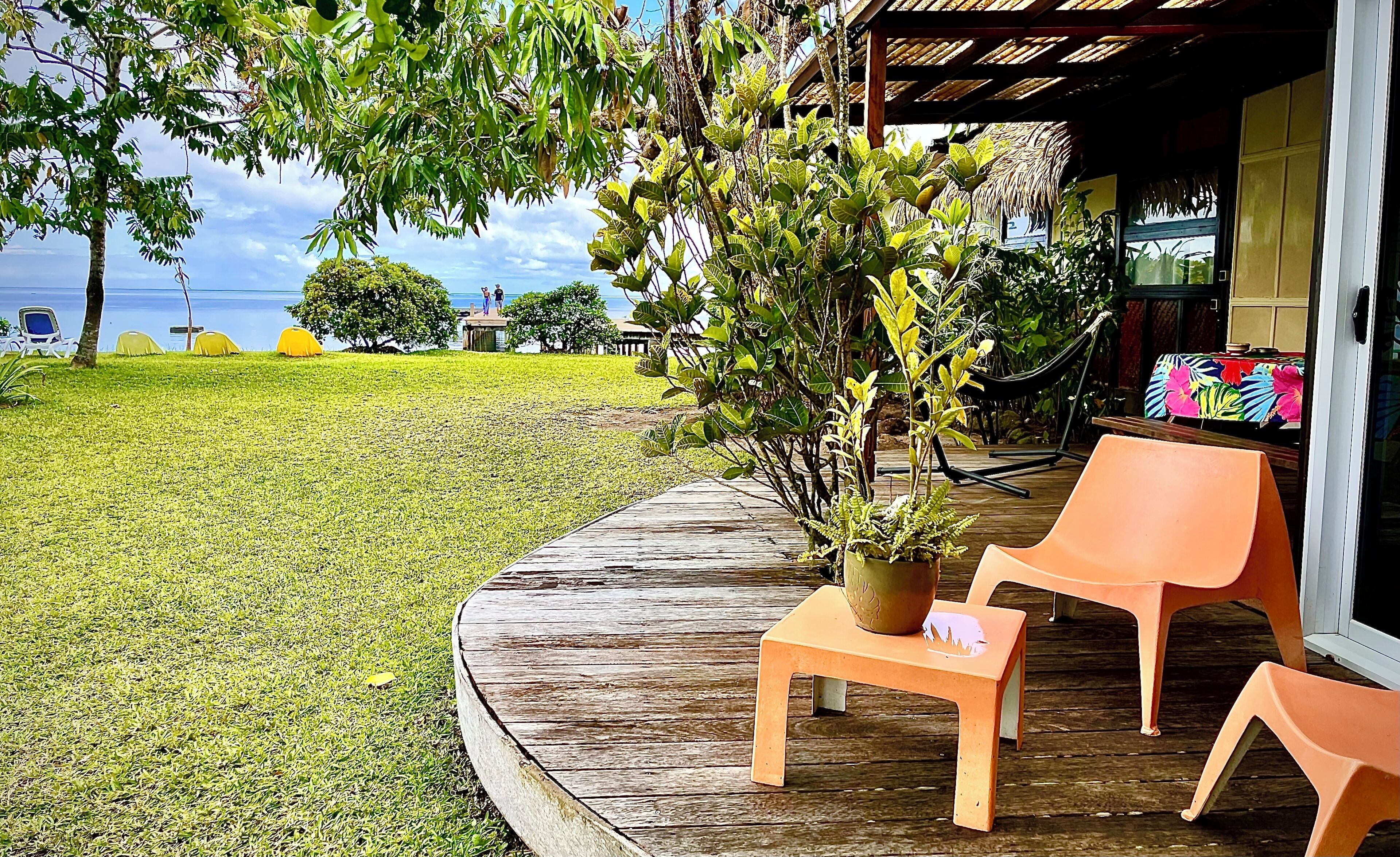 Um deck de madeira com mesa e cadeiras, um vaso de planta e vista para o mar.