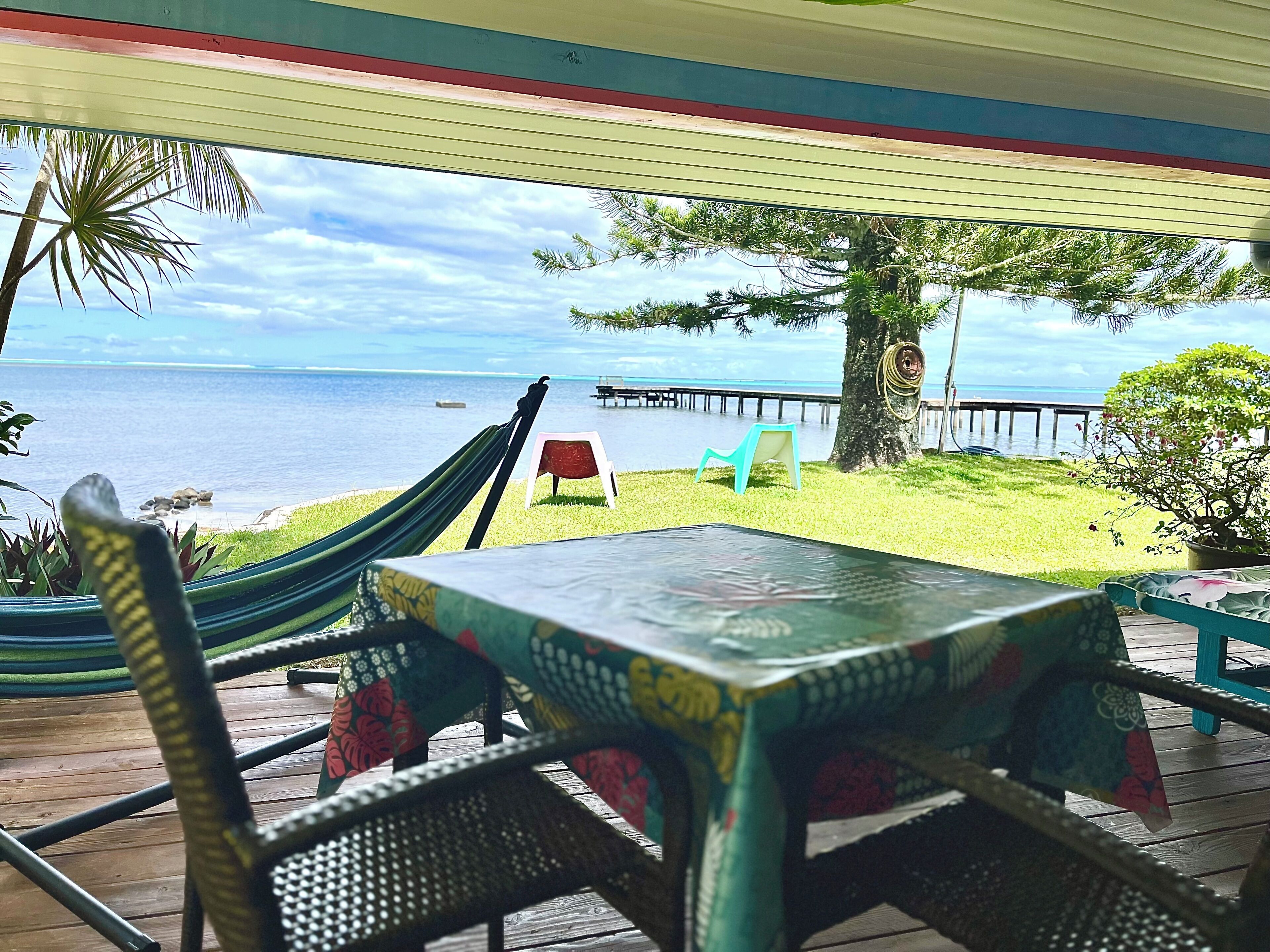 A covered outdoor seating area with a table and chairs, overlooking a beach and the ocean.