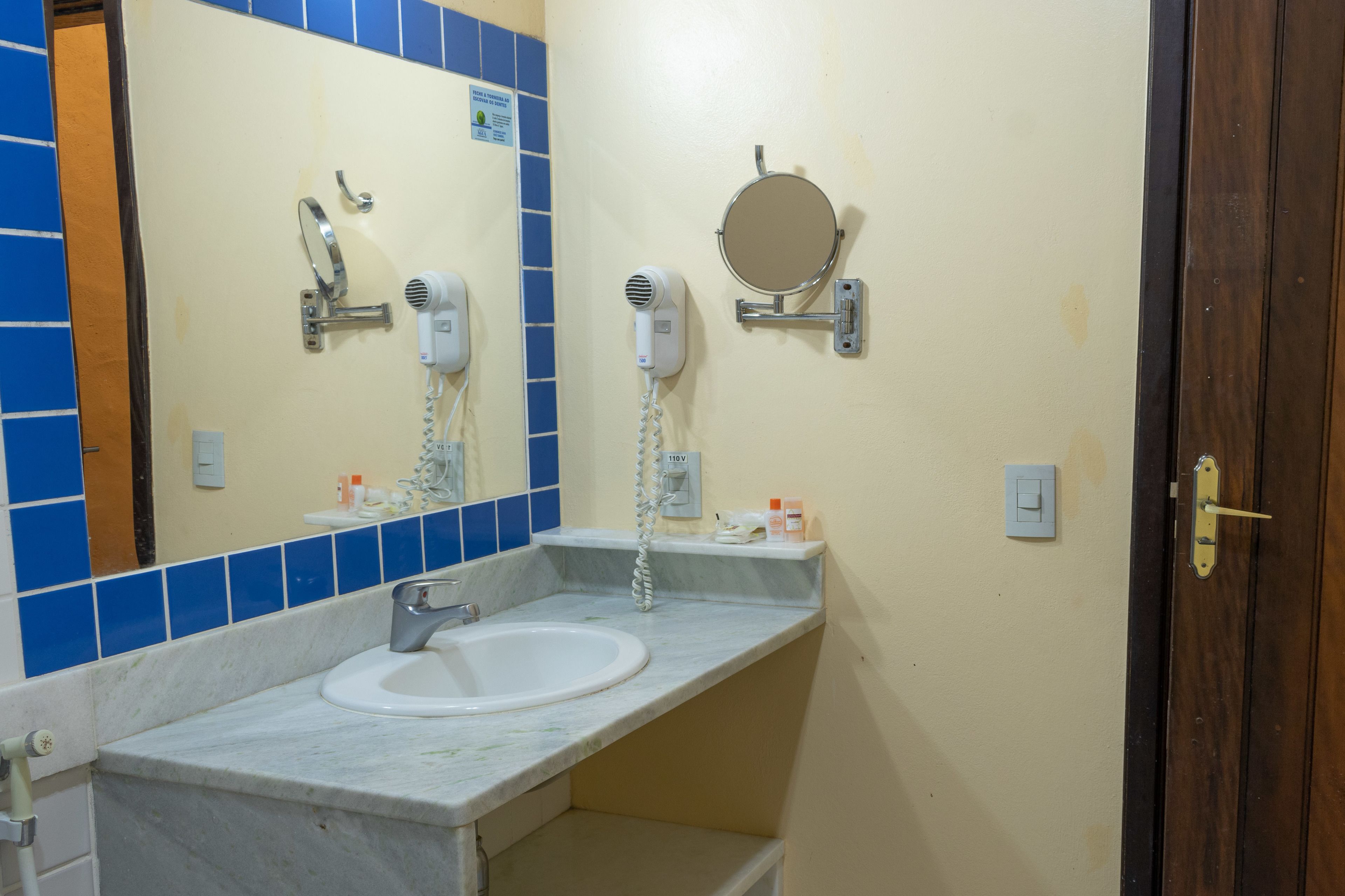 Un baño con lavamanos, espejo, secador de pelo y toallero.