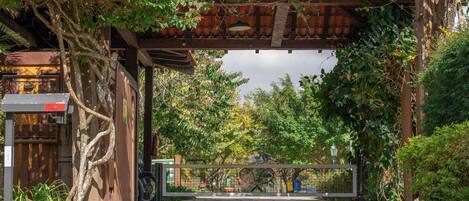A gated entrance with a wooden pergola, a bicycle, and a building with a tiled roof.