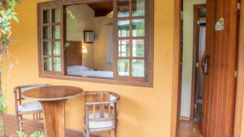 A room with a wooden table and two chairs, a window with a view of the interior, and a door with a number sign.