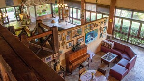 Un interior espacioso con una escalera de madera, un sofá rojo, un piano y un comedor con una mesa dispuesta para dos.