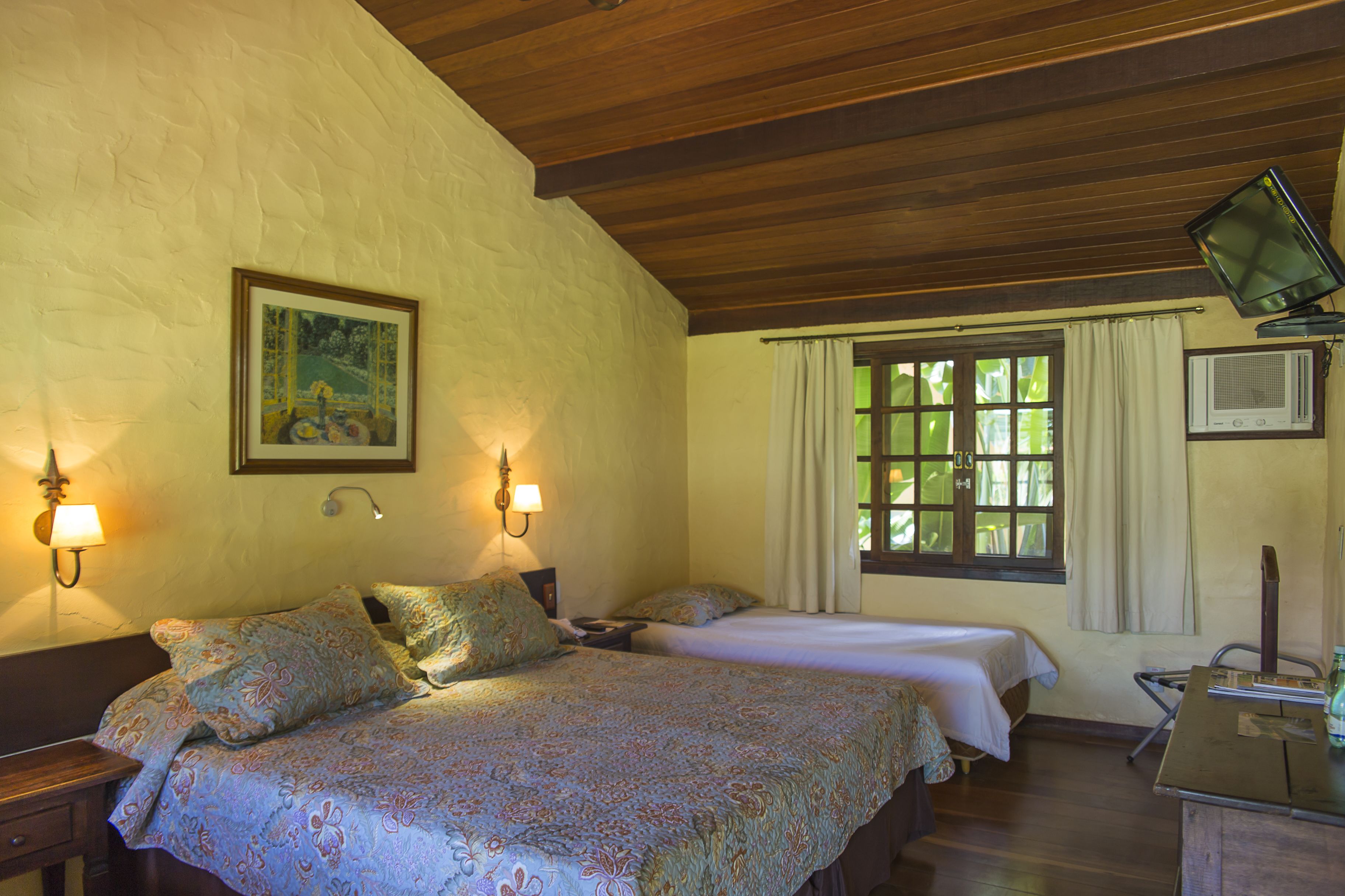 Quarto com duas camas, teto de madeira, um quadro na parede e janela com cortinas.