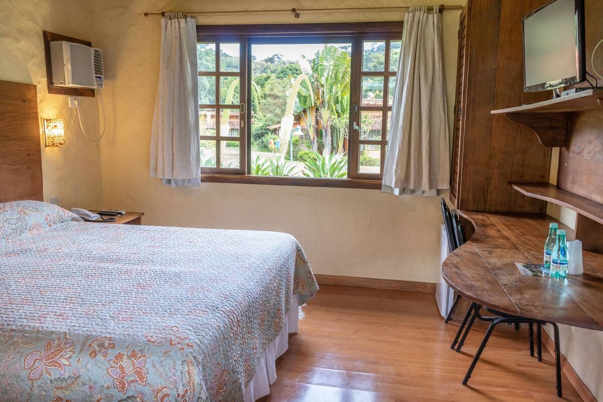 A bedroom with a bed, a desk, a chair, and a window with curtains.