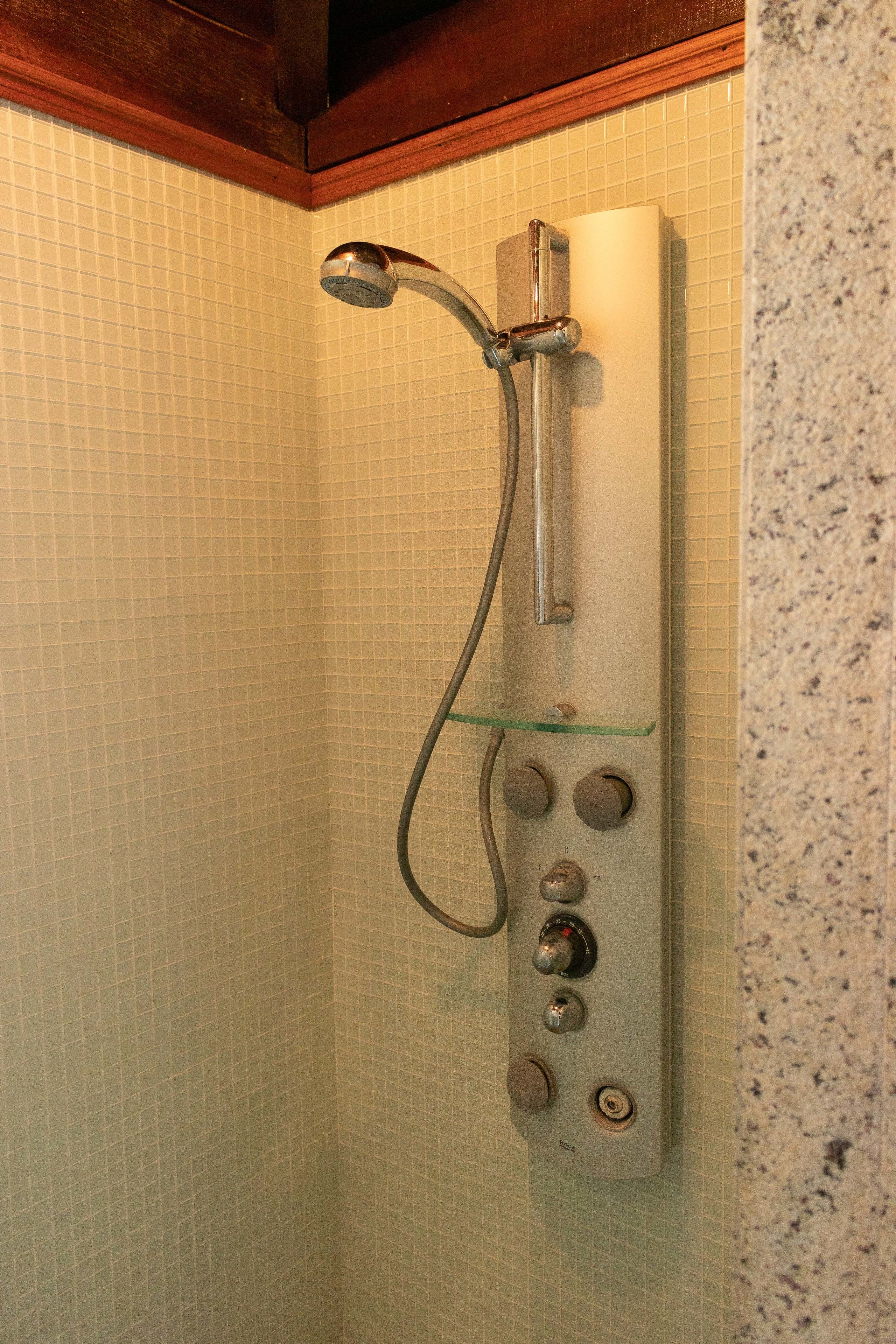 A shower with a handheld showerhead and control knobs.
