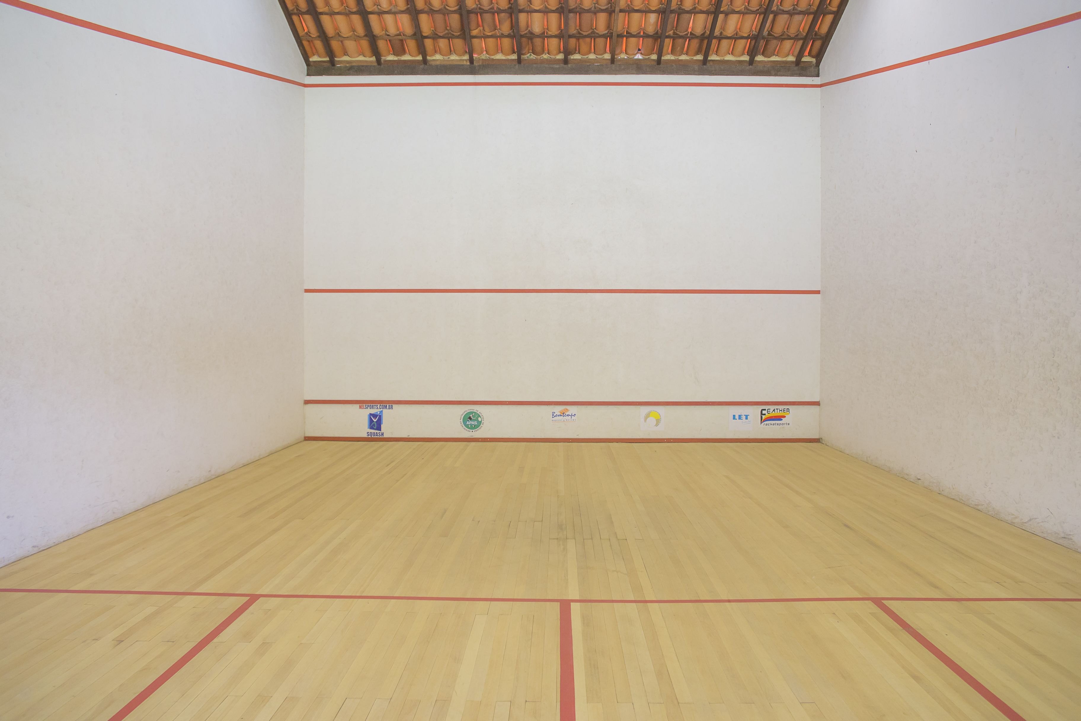 Una cancha de squash con piso de madera y líneas delimitadoras rojas.