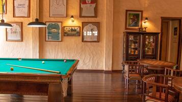 A billiards table with balls and cues, a pool table, wooden chairs, and framed pictures on the wall.