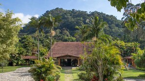 A tropical resort with a stone pathway leading to a building with a tiled roof, surrounded by lush greenery and palm trees. - Hotel Bomtempo Itaipava (Petrópolis)