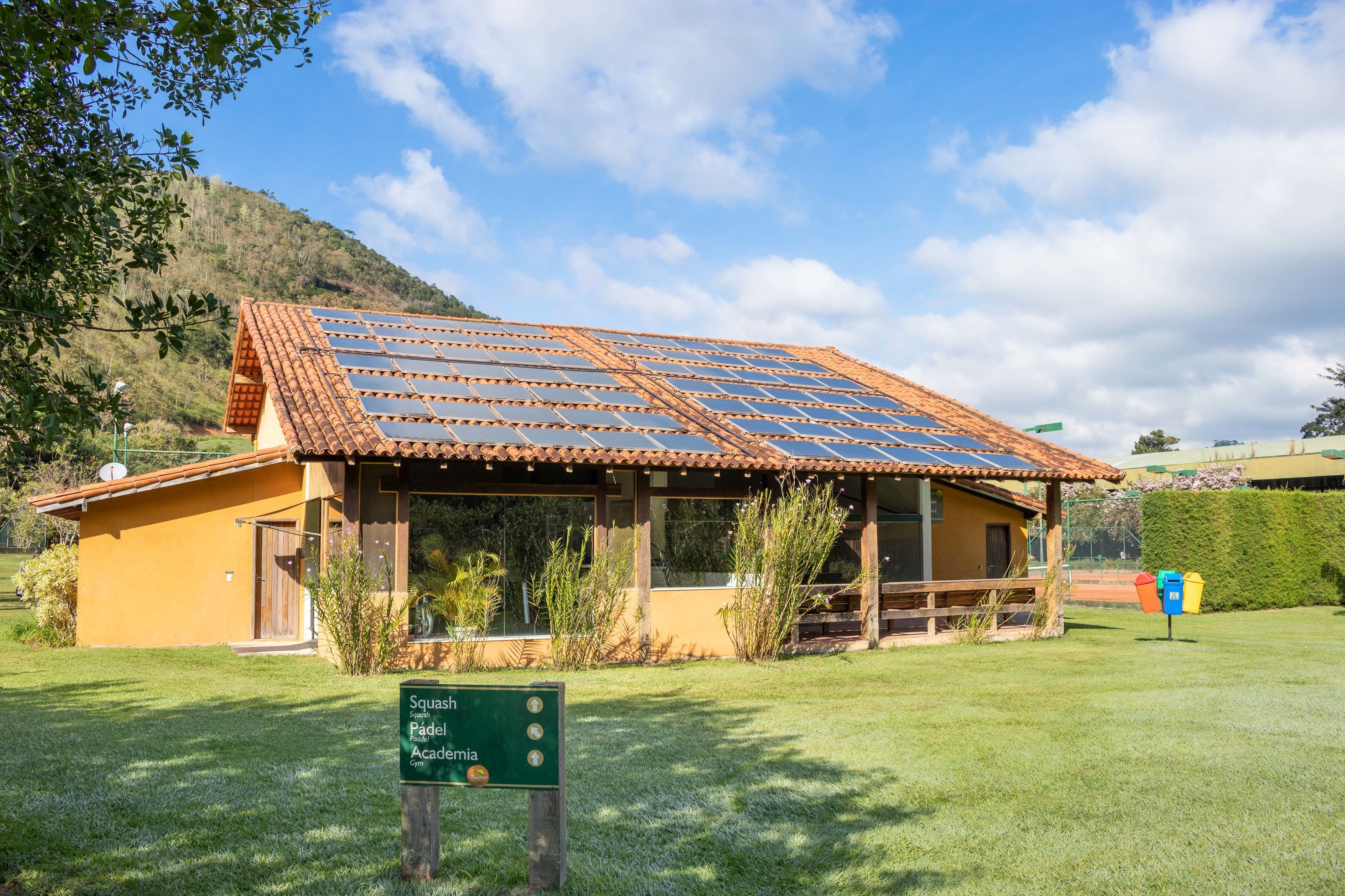 A building with a tiled roof and solar panels, surrounded by greenery and a sign indicating it is a Squash facility.