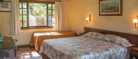A room with two beds, a wooden desk, a window with curtains, and a painting on the wall.