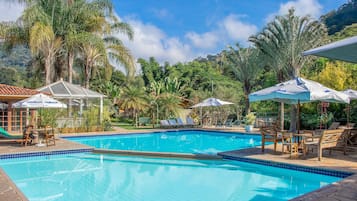 Una piscina al aire libre, sombrillas, sillones reclinables de piscina