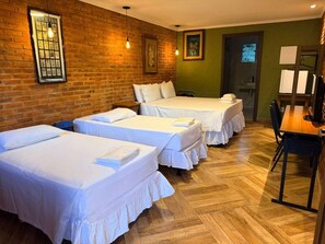 Habitación de hotel con tres camas, suelo de madera, pared de ladrillo y un cuadro enmarcado.