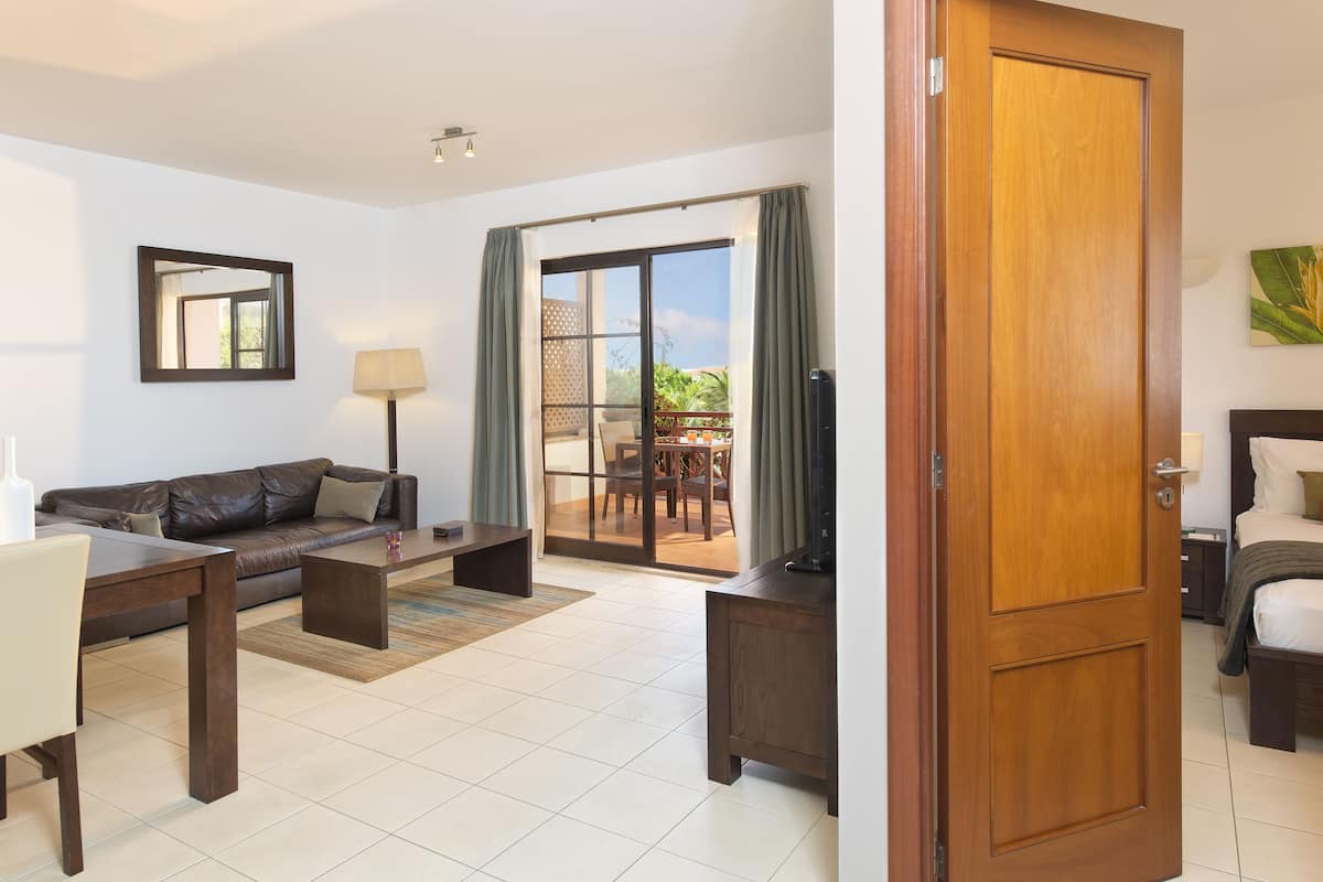 A hotel room with a sofa, a coffee table, a TV, a bed, and a sliding glass door leading to an outdoor area.