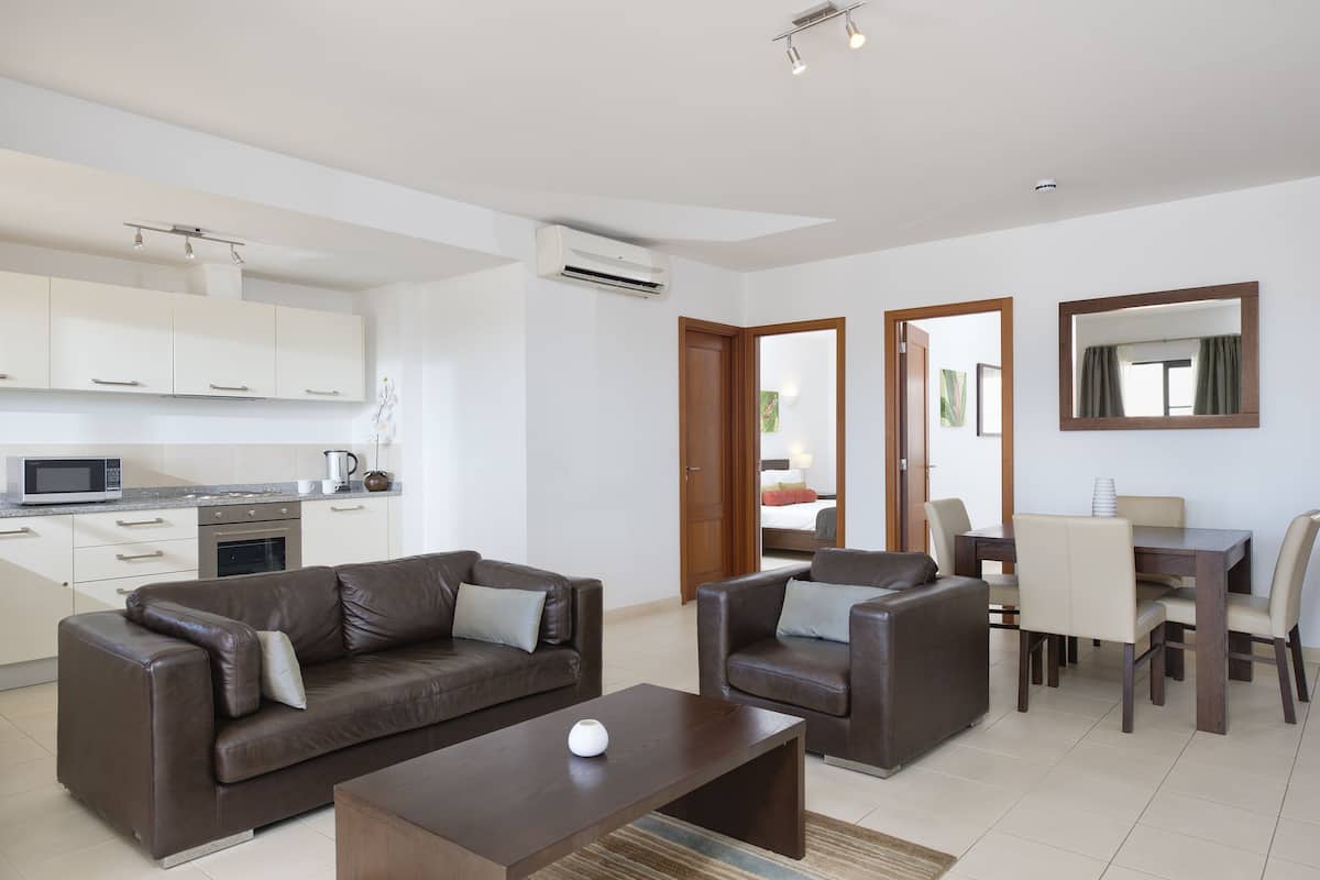 A modern living room with a brown leather sofa, a wooden coffee table, and a dining area with a wooden table and chairs.