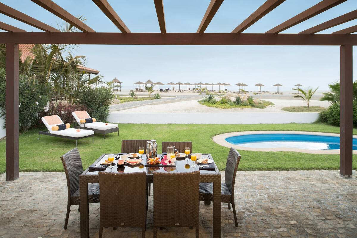 An outdoor dining area with a table set for breakfast, overlooking a pool and beach.