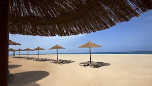 Una spiaggia con ombrelloni di paglia e sdraie, un cielo sereno e l'oceano sullo sfondo.
