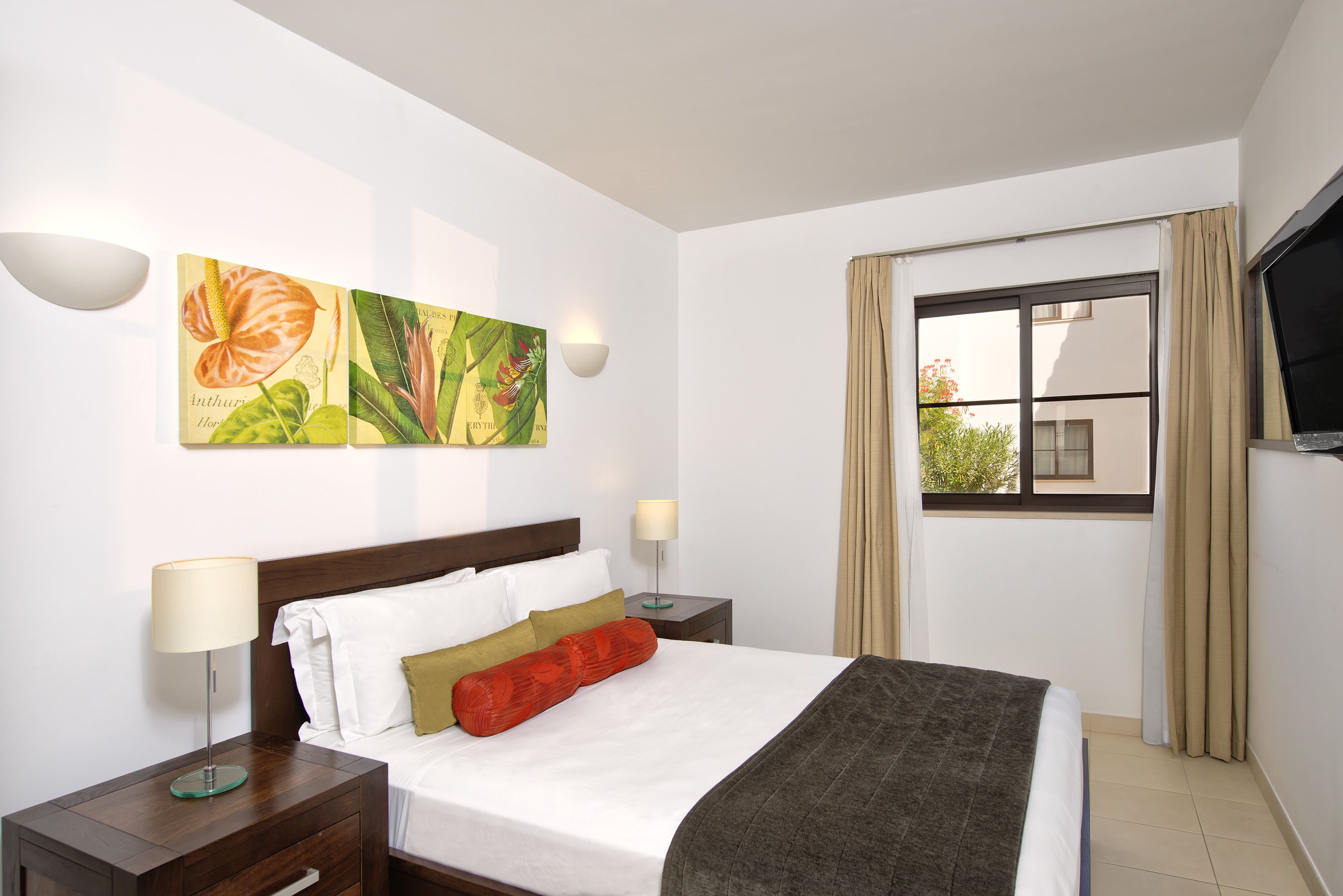 Een hotelkamer met een bed, twee nachtkastjes, een aan de muur bevestigde televisie en een raam met gordijnen.