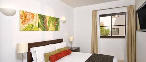 Een hotelkamer met een bed, twee nachtkastjes, een aan de muur bevestigde televisie en een raam met gordijnen.