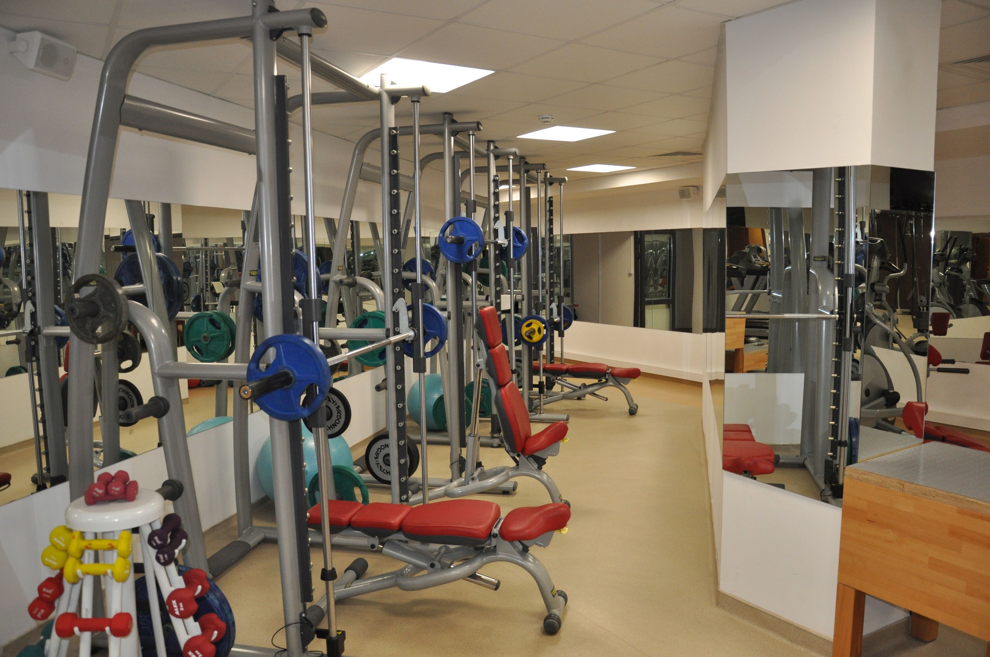 Una palestra con diverse attrezzature per sollevamento pesi, panche e specchi.