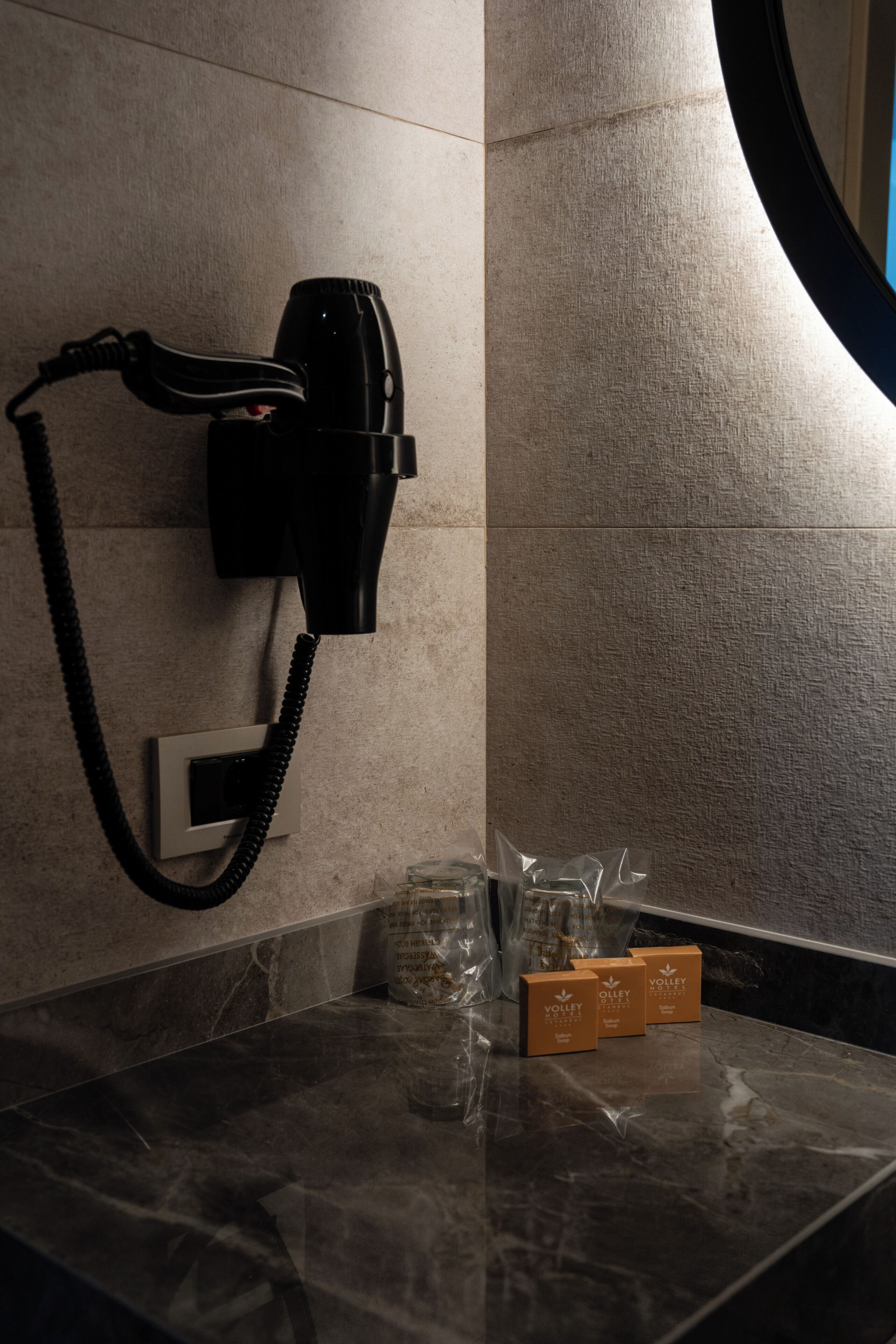 A bathroom with a hairdryer mounted on the wall, a marble countertop, and toiletries in plastic bags.