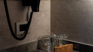 A bathroom with a hairdryer mounted on the wall, a marble countertop, and toiletries in plastic bags.