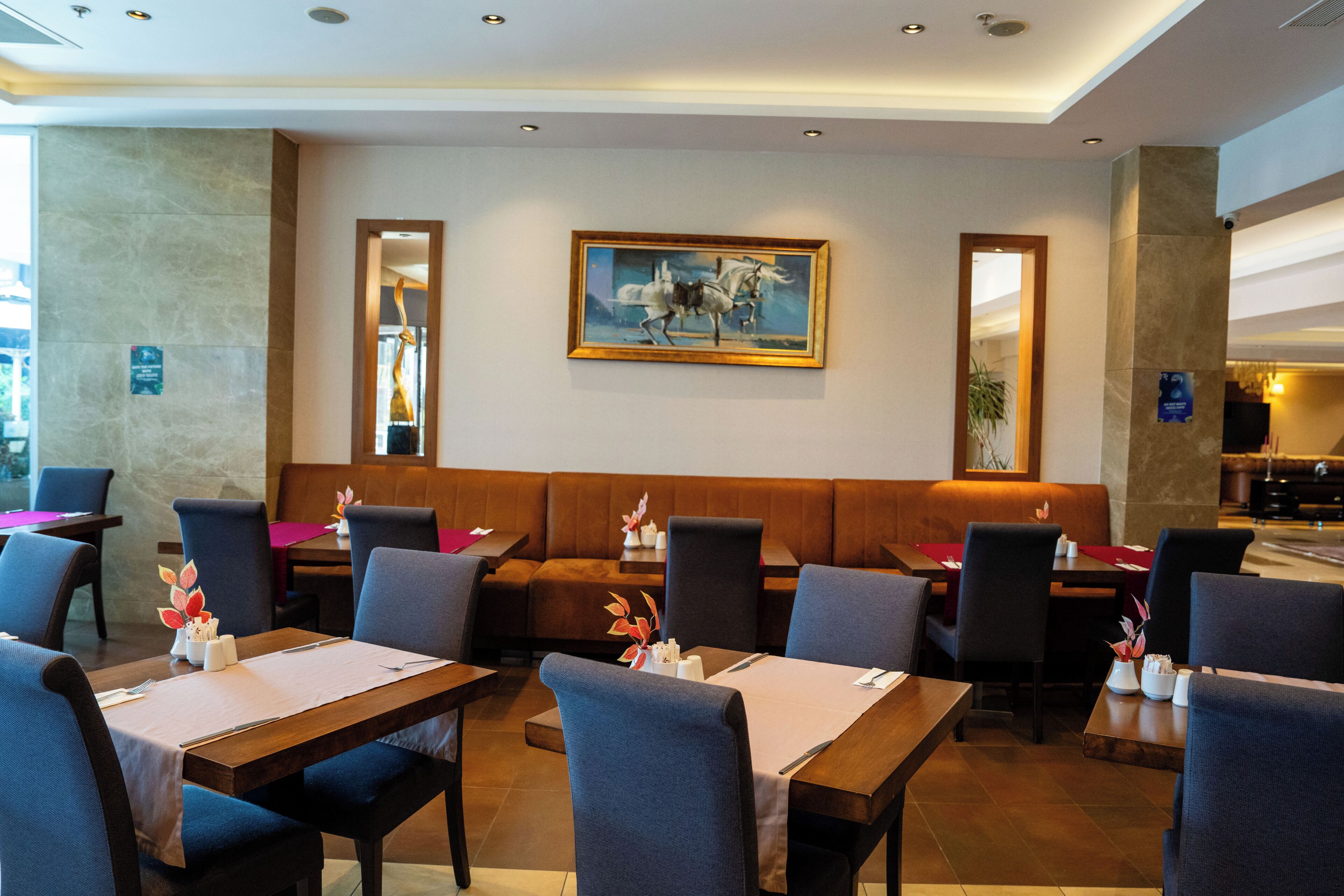 Um restaurante com cabines, mesas e cadeiras, exibindo uma pintura na parede.